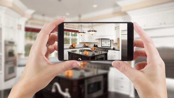A color photo of hands holding a phone looking at an image of the room they are in