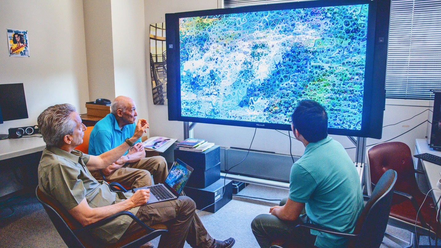 Three people looking at a digital image on large screen