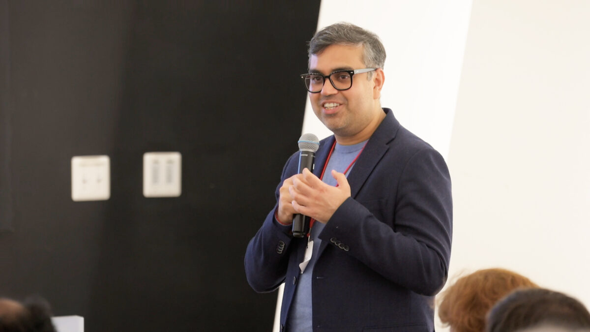 A color photo of a man talking into a microphone