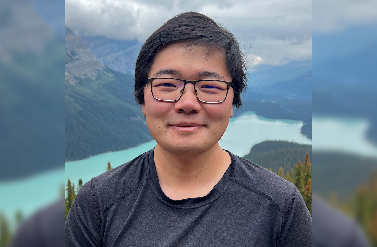 A color photo of a man smiling for a photo outside.